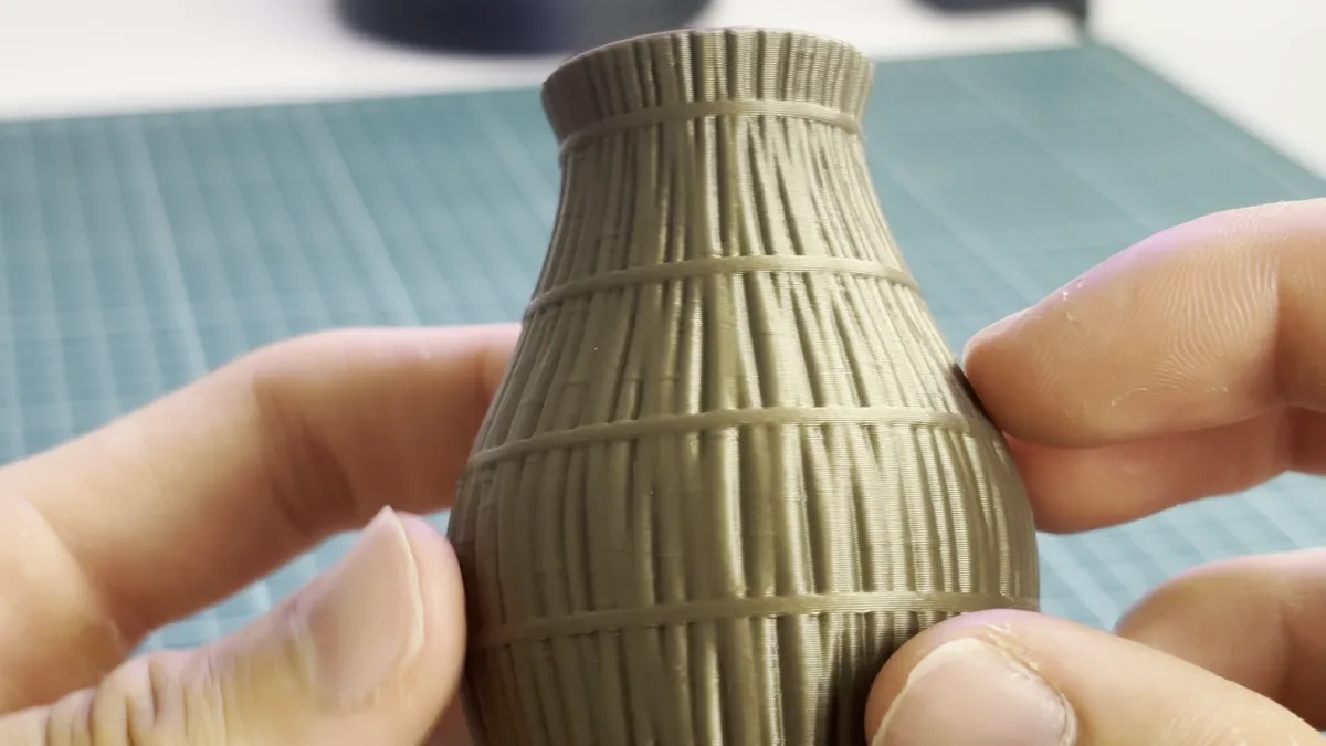 Jarrón impreso en 3D en PLA marrón con textura de cañas en vertical y anillos, sujeto con las dos manos