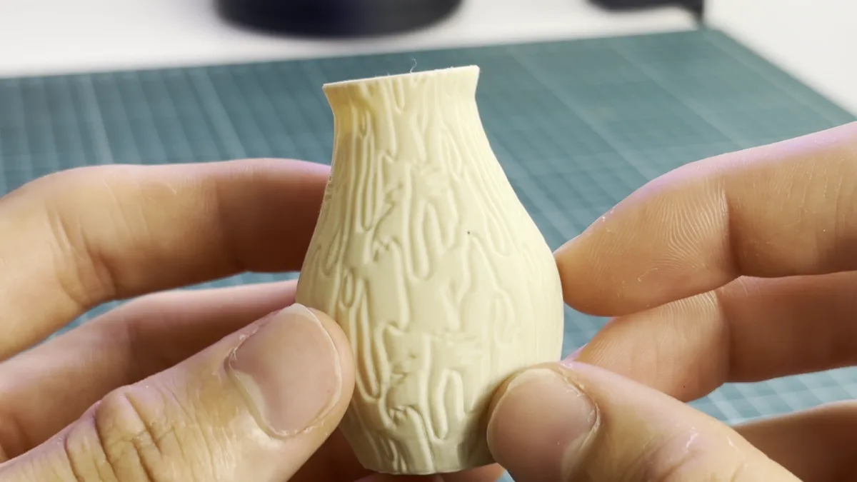 Jarrón pequeño impreso en 3D en PLA crema con la textura Corteza, sujeto con dos dedos