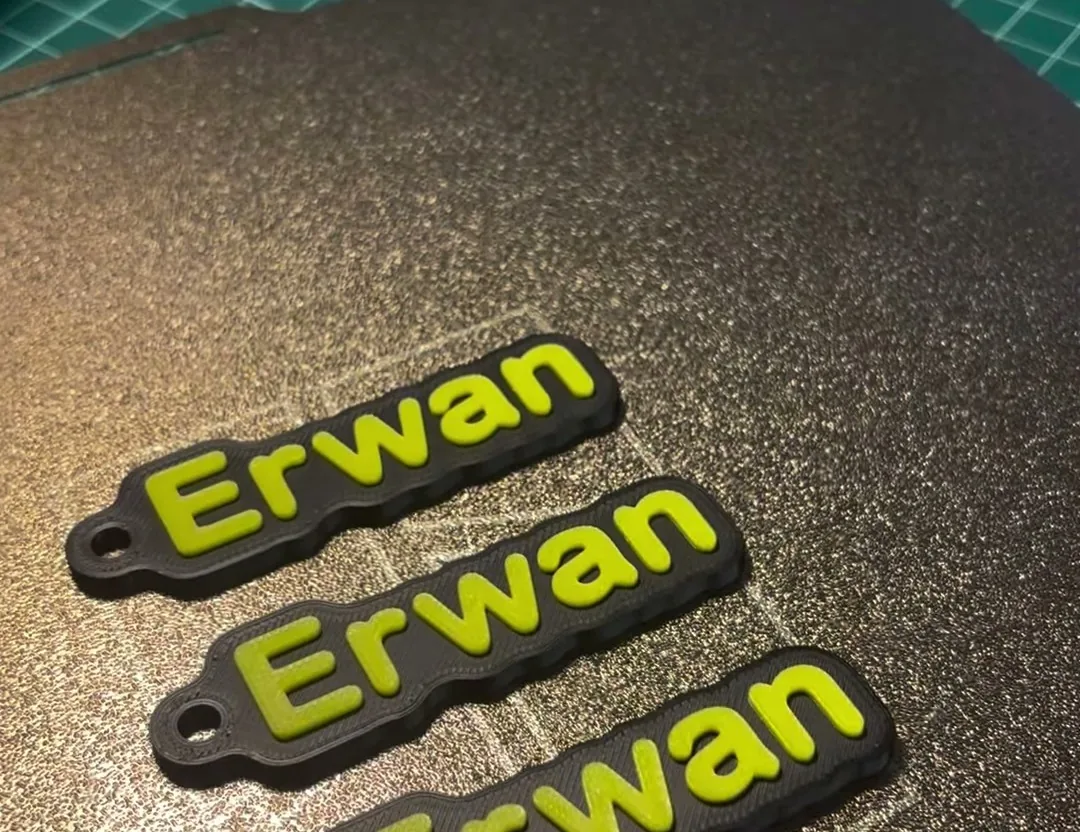 Tres llaveros negros con el nombre Erwan en relieve amarillo, lisos y sin huecos, sobre la placa de impresión