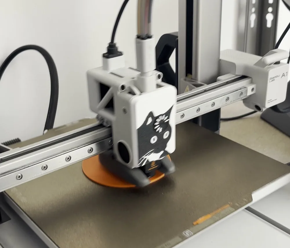 Bambu Lab A1 imprimiendo la primera capa de una pieza redonda naranja sobre una placa texturizada