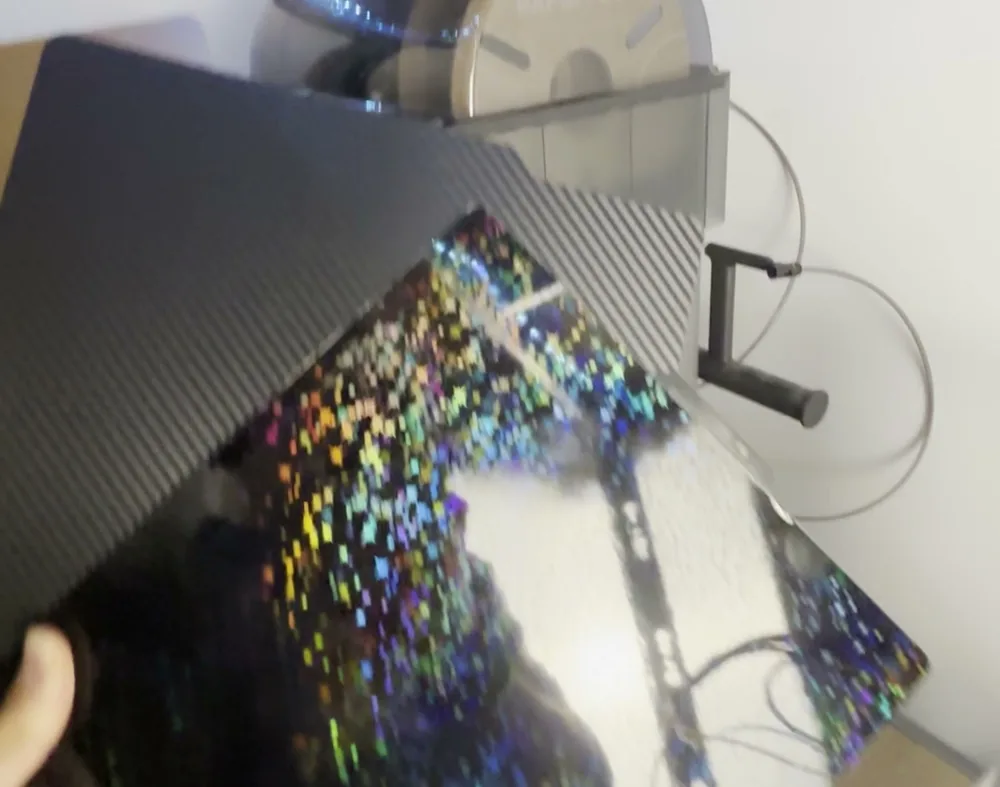 Placa de impresión lisa y brillante con destellos de colores tipo estrellas, sujeta en la mano delante de una placa de fibra de carbono