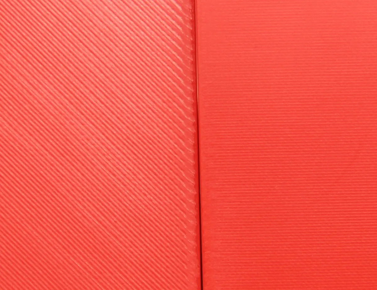 Dos tarjetas rojas impresas en 3D, una al lado de la otra: la de la izquierda sin planchar, con las líneas de la última capa en diagonal, y la de la derecha planchada y lisa