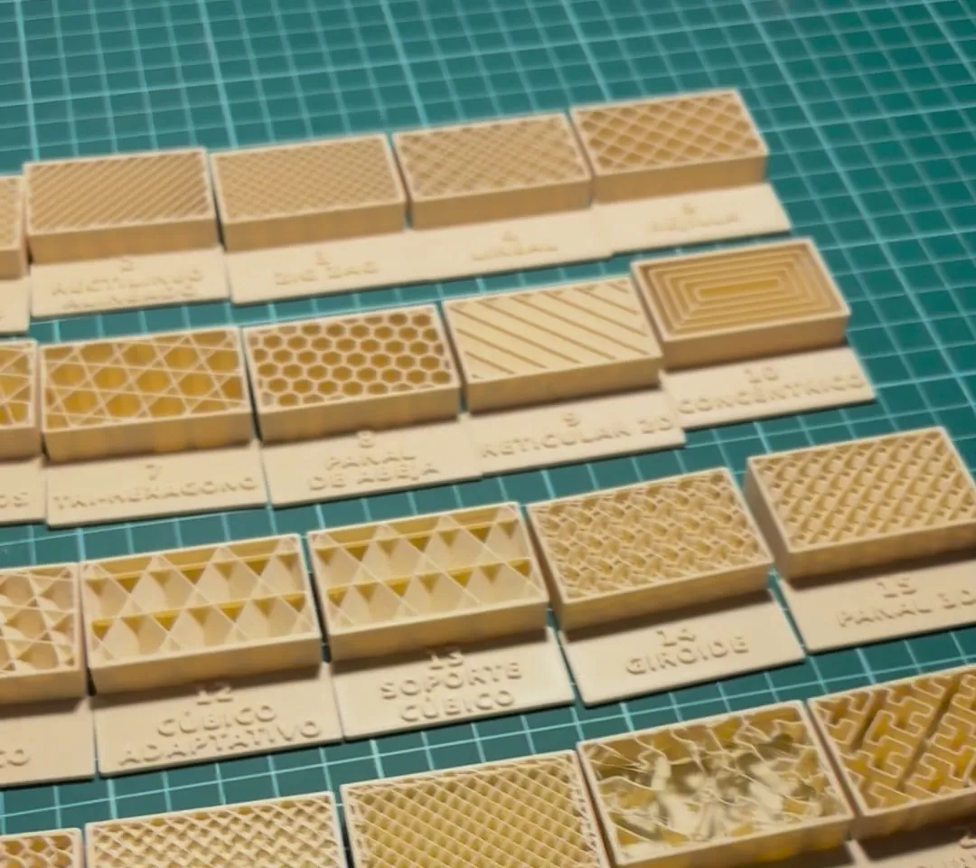 Los 22 bloques del muestrario de rellenos impresos en PLA crema sobre una alfombrilla de corte, sin tapa, cada uno con el dibujo de su relleno y su nombre delante