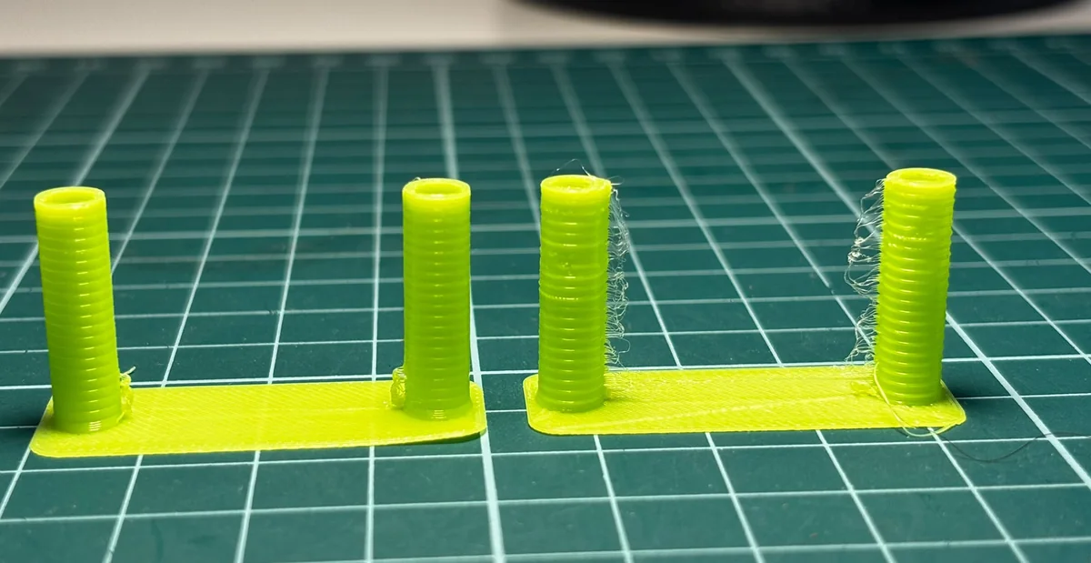 Dos torres del test de retracción en TPU amarillo sobre una alfombrilla de corte: la de la izquierda casi limpia y la de la derecha con hilos en las dos torres