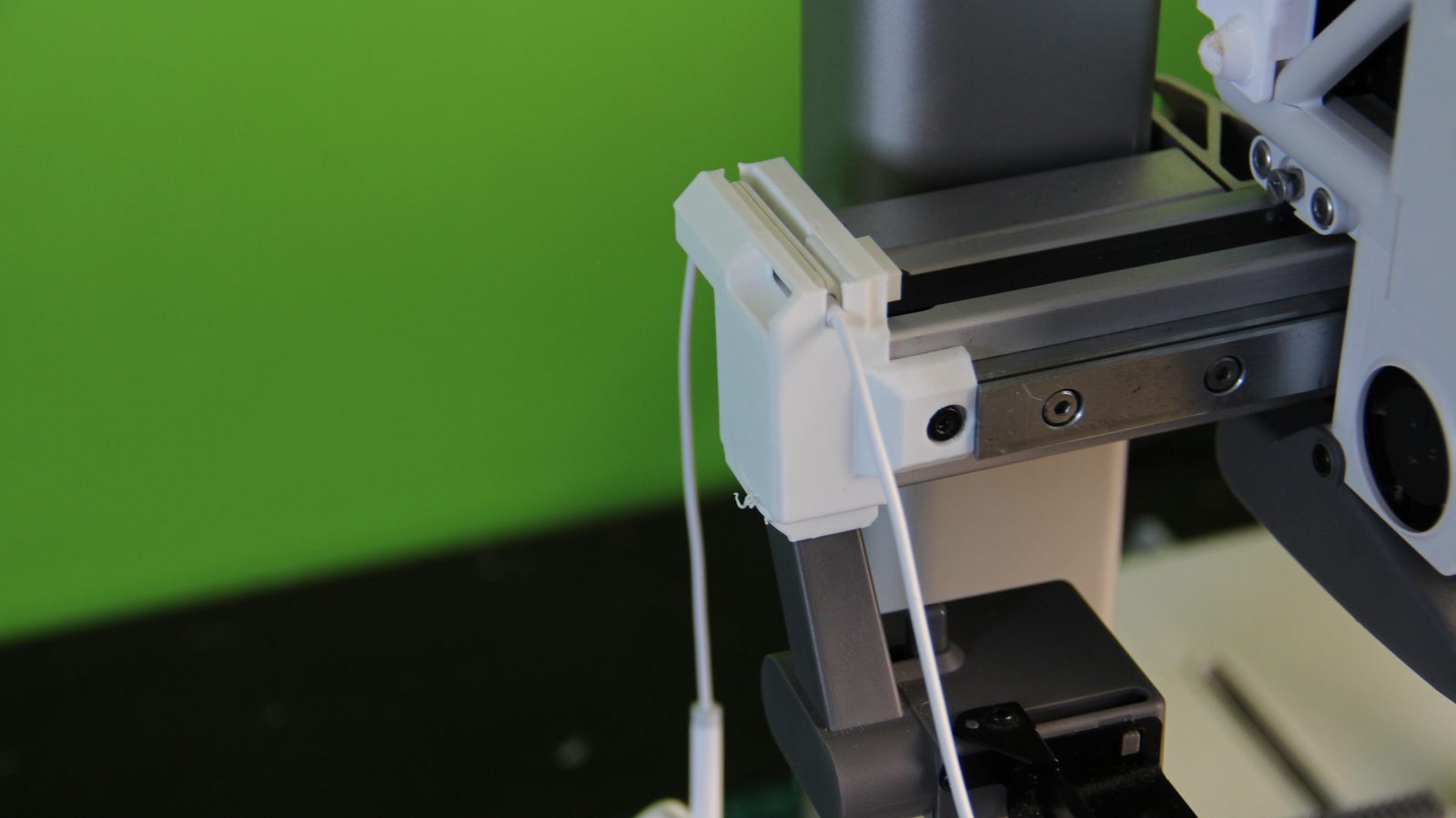 El móvil en un trípode delante de la Bambu Lab A1, con unos auriculares de cable blancos enchufados