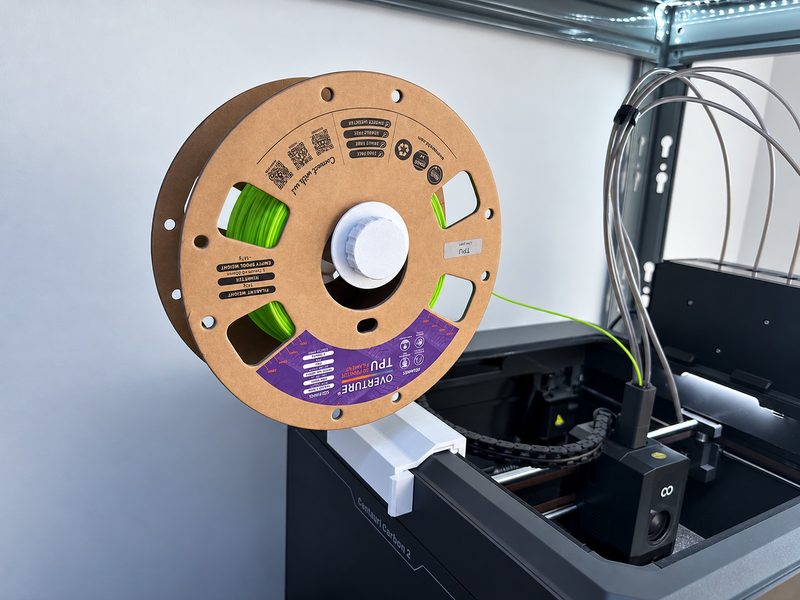 La v2 del soporte de bobina, impresa en blanco, con una bobina de TPU en el lateral de la Elegoo Centauri Carbon 2