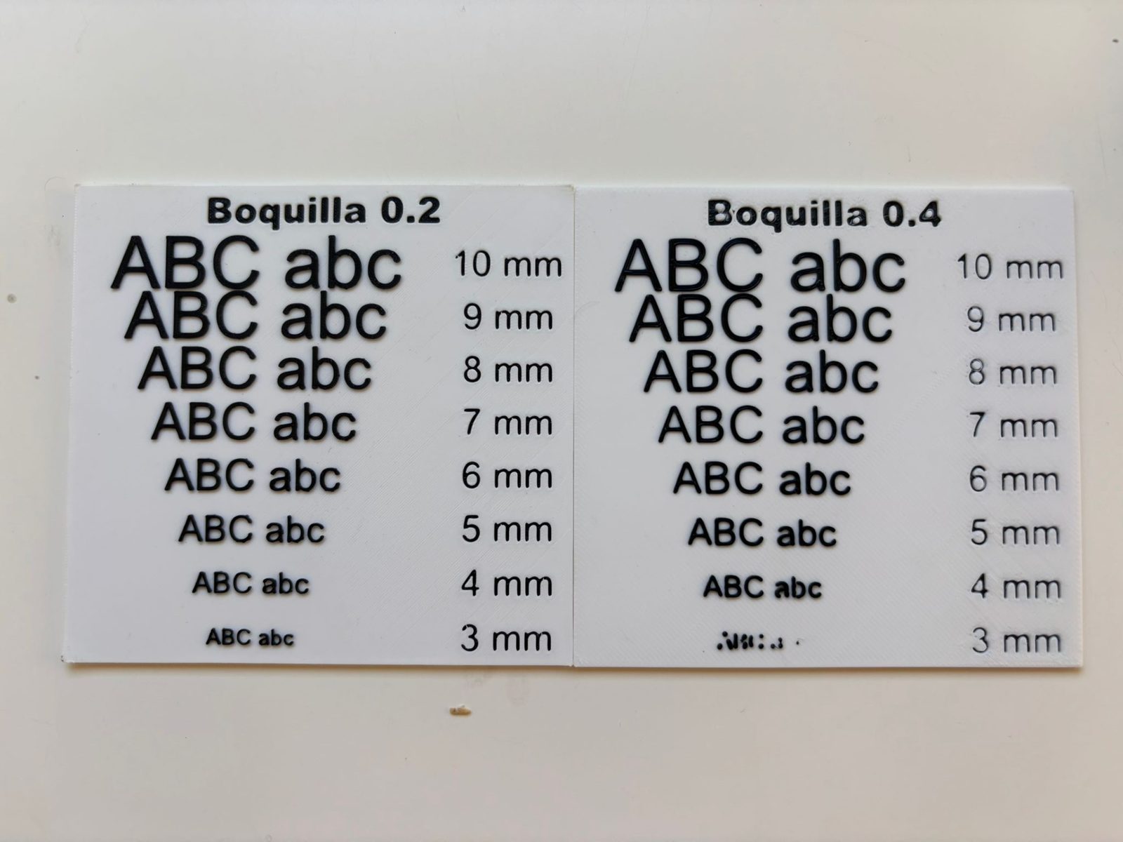 Las dos placas del test impresas en PLA blanco con letras negras: a la izquierda la de boquilla 0.2 y a la derecha la de 0.4